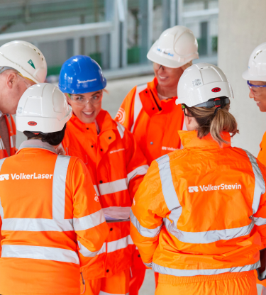 Group of six people all wearing orange PPE, stood talking/looking at each other