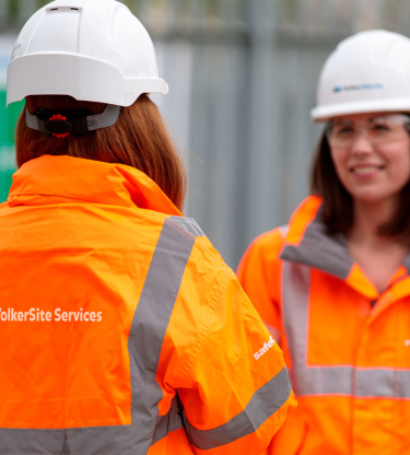 Two female employees in orange PPE and white hardhats